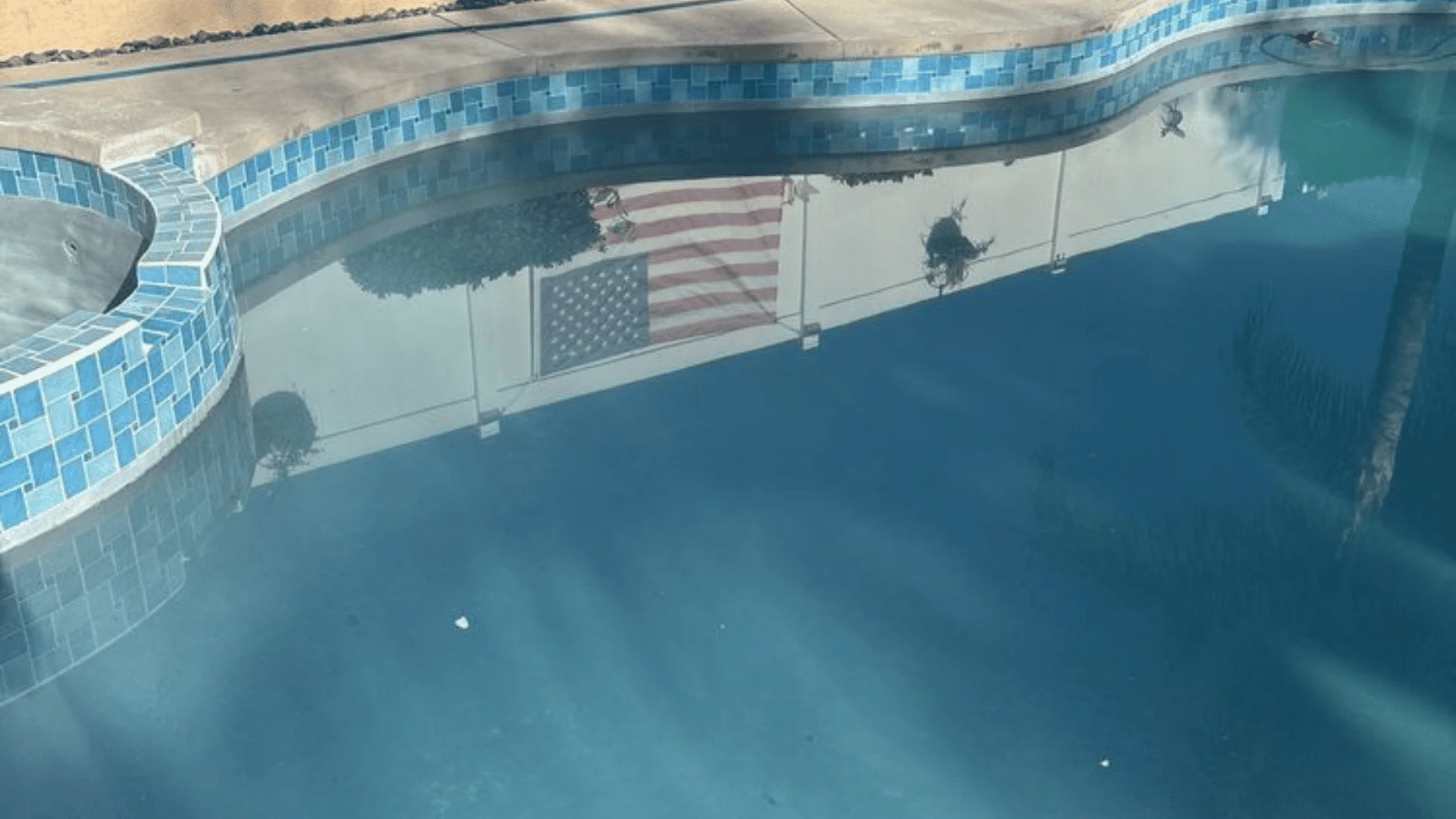 A clear, blue residential swimming pool in a Rialto, CA backyard after a monthly maintenance service visit. A pool technician checks equipment near the pool deck on a sunny Southern California day.