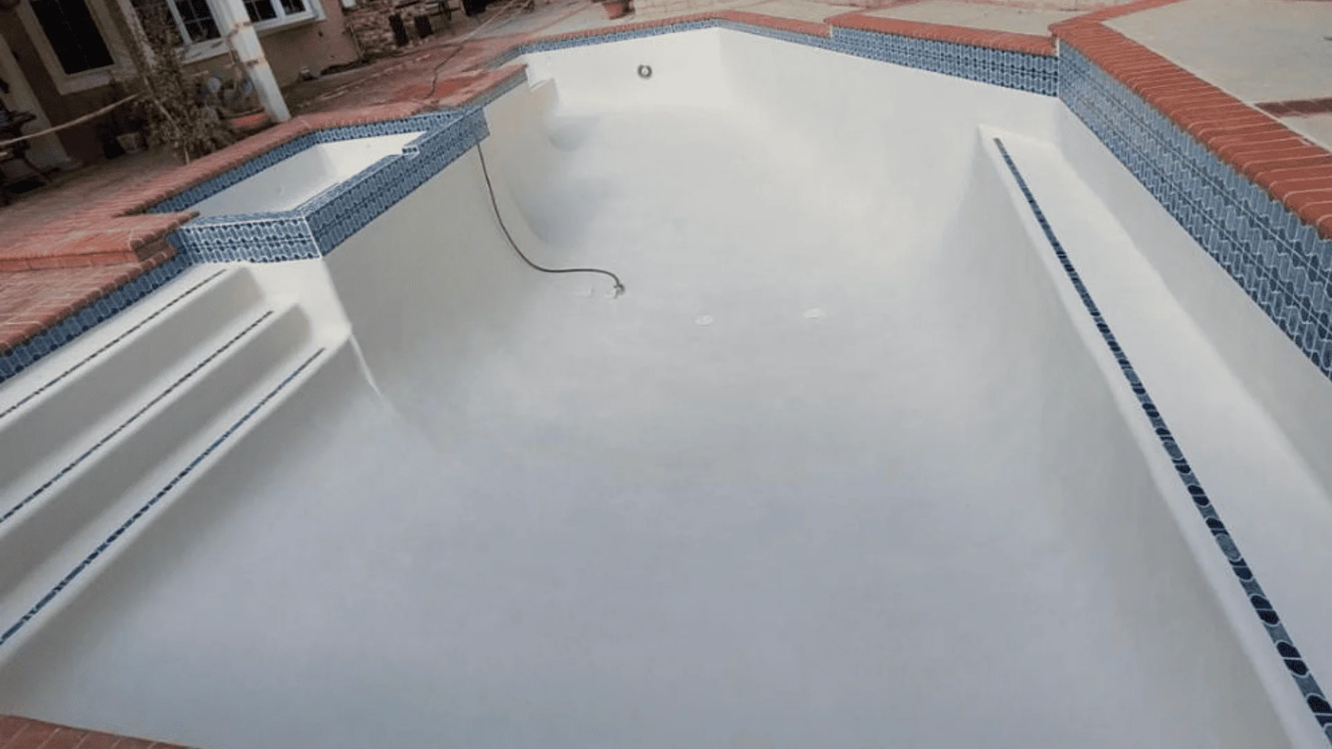 A freshly remodeled backyard swimming pool in Rialto, CA with new plaster surface, updated tile coping, and a clean concrete deck. The pool is filled with clear water under a sunny Inland Empire sky.